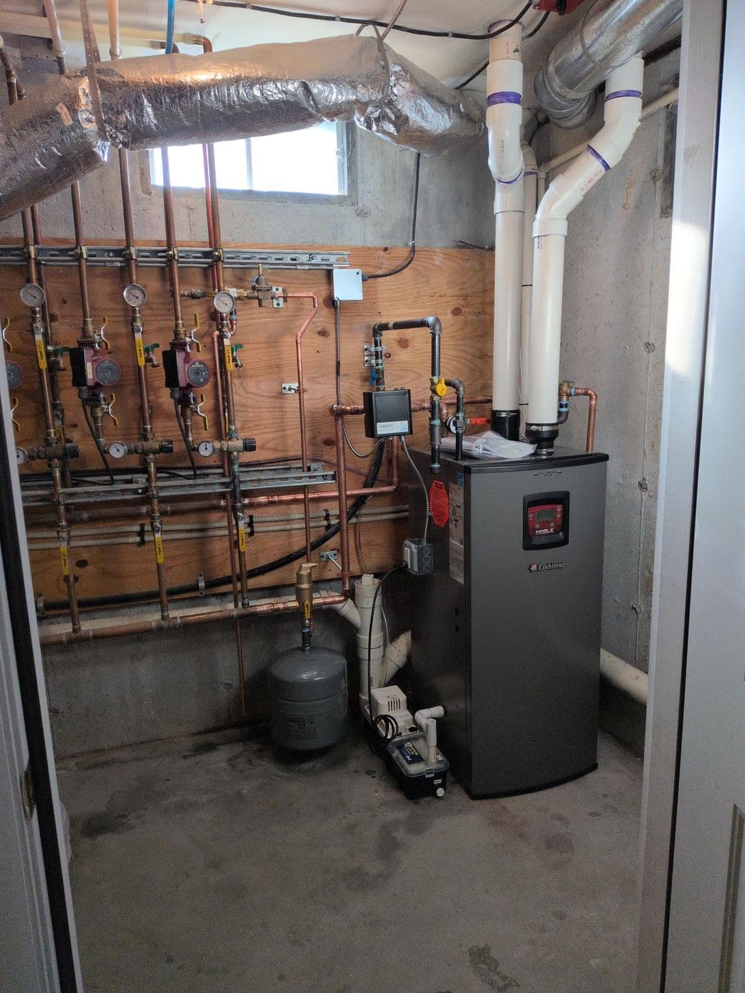 High-efficiency condensing boiler beside a multi-zone copper manifold in a basement mechanical room